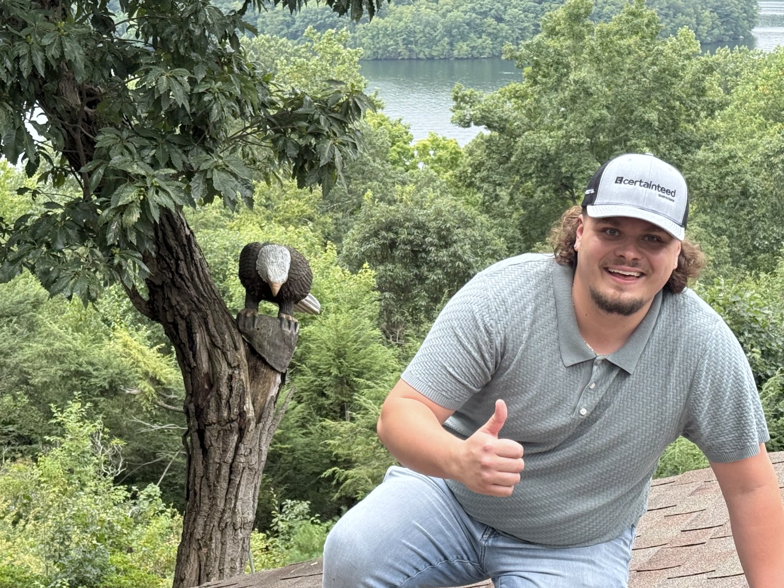 Szymon Pogorzelski on the roof of one of Eagle Heights' first jobs, with the customer's carved eagle in the tree beside him