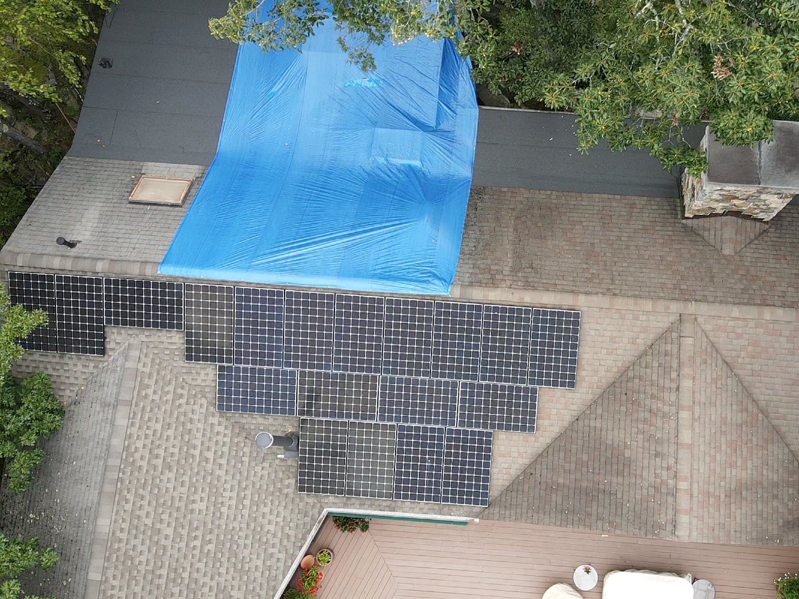 Drone view of a roof with a solar array, a tarped leak above it and a vent stack between the panels